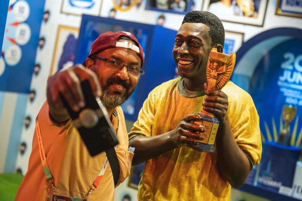 A fan poses for a selfie photograph with a statue of the Brazilian football legend Pele in Doha on December 6, 2022, during the Qatar 2022 World Cup football tournament. (Photo by ANDREJ ISAKOVIC / AFP)