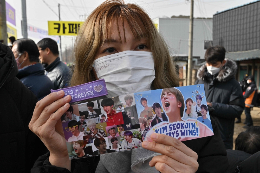 A fan holds pictures of BTS singer Jin in front of a military training unit in Yeoncheon on December 13, 2022, as the place where BTS singer Jin is scheduled to arrive to begin his military service. Photo by Jung Yeon-je / AFP