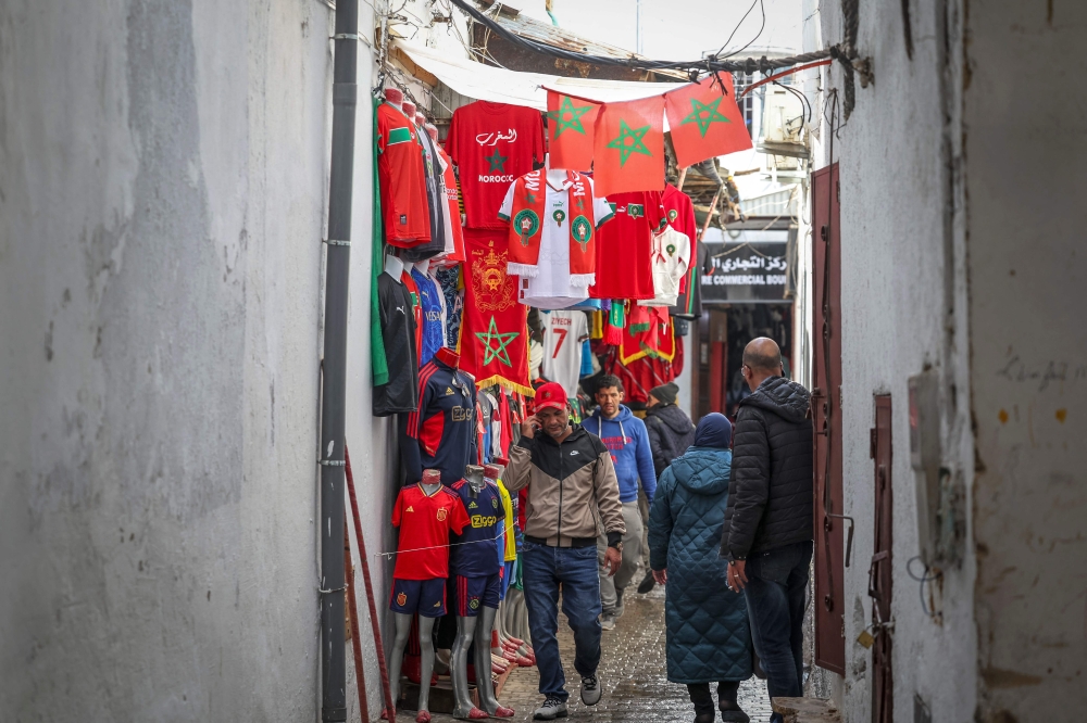 People walk past a sports apparel shop in Morocco's capital Rabat on December 13, 2022 a day ahead of the Qatar 2022 FIFA World Cup semi-final football match between Morocco and France. (Photo by FADEL SENNA / AFP)