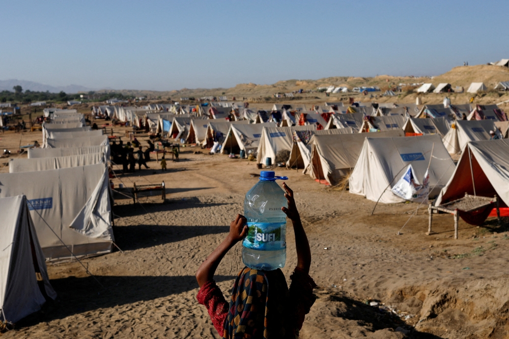 A displaced girl carries a bottle of water she filled from nearby stranded flood-waters, as her family takes refuge in a camp, in Sehwan, Pakistan, September 30, 2022. (REUTERS/Akhtar Soomro)