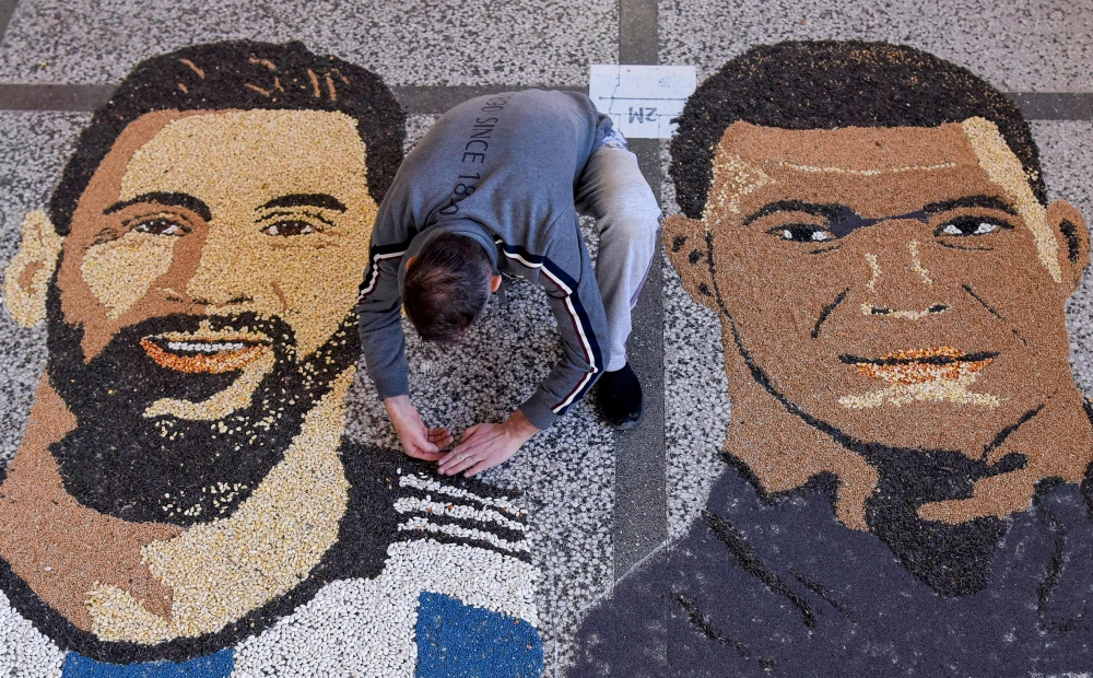 Kosovar artist Alkent Pozhegu works on the last details of his mosaic, made with grain and seeds on the ground, depicting Argentina's forward Lionel Messi (left) and France's forward Kylian Mbappe in the town of Gjakova on December 17, 2022, on the eve of the Qatar 2022 World Cup final match between Argentina and France. (Photo by Armend NIMANI / AFP) 