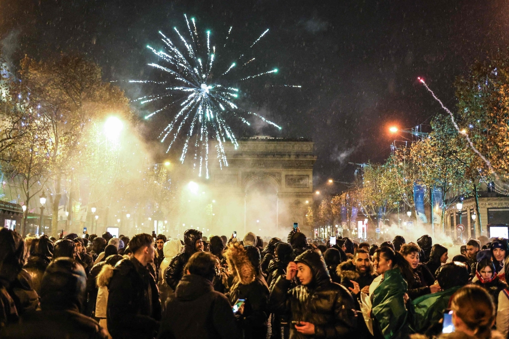 Fireworks explode overhead as people gather on the Champs-Elysees after the final football match of the Qatar 2022 World Cup between Argentina and France in central Paris on December 18, 2022. (Photo by Charly Triballeau / AFP)
 