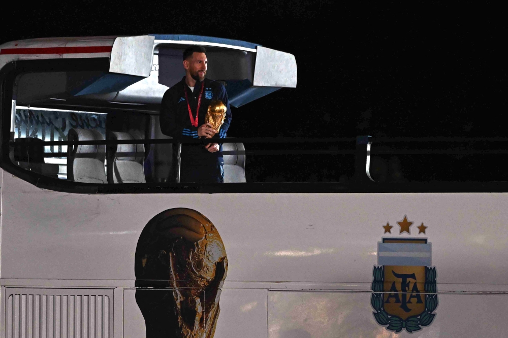 Argentina's captain and forward Lionel Messi holds the FIFA World Cup Trophy on board a bus upon arrival at Ezeiza International Airport on December 20, 2022. (Photo by Luis Robayo / AFP)