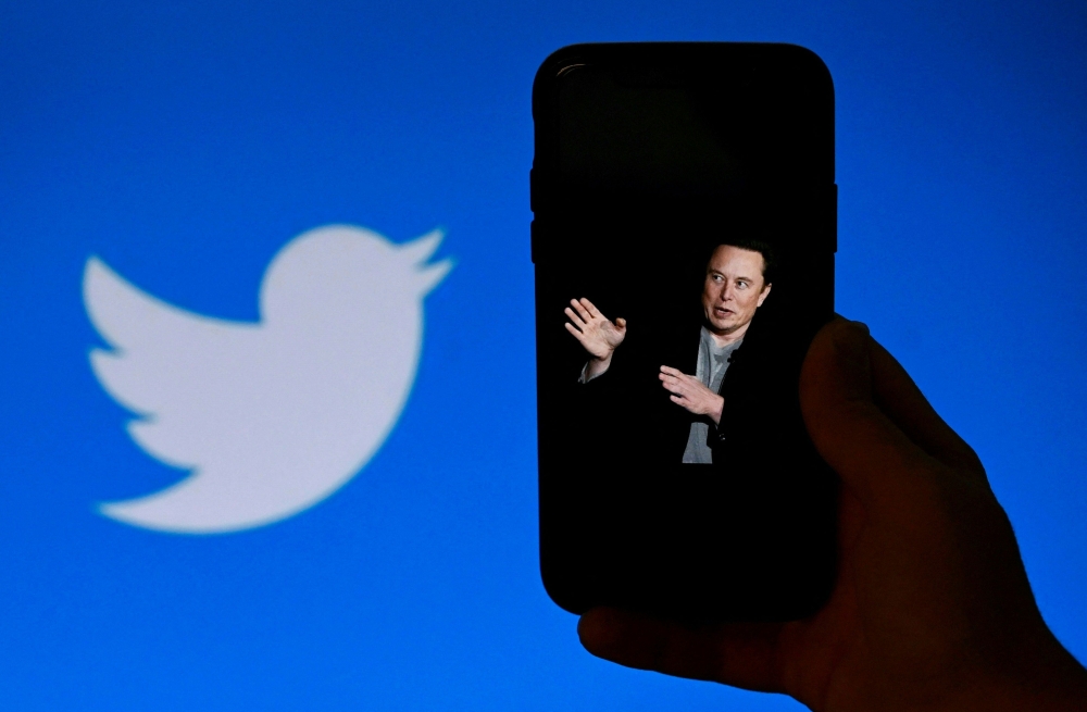 In this file photo taken on October 4, 2022, a phone screen displays a photo of Elon Musk with the Twitter logo shown in the background, in Washington, DC. Photo by Olivier Douliery / AFP)