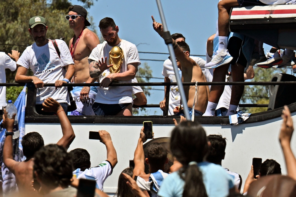 Argentina's Lionel Messi waves at fans holding the FIFA World Cup Trophy as the team parades on board a bus after winning the Qatar 2022 World Cup tournament in Buenos Aires, Argentina on December 20, 2022.  (Photo by Luis ROBAYO / AFP)
 