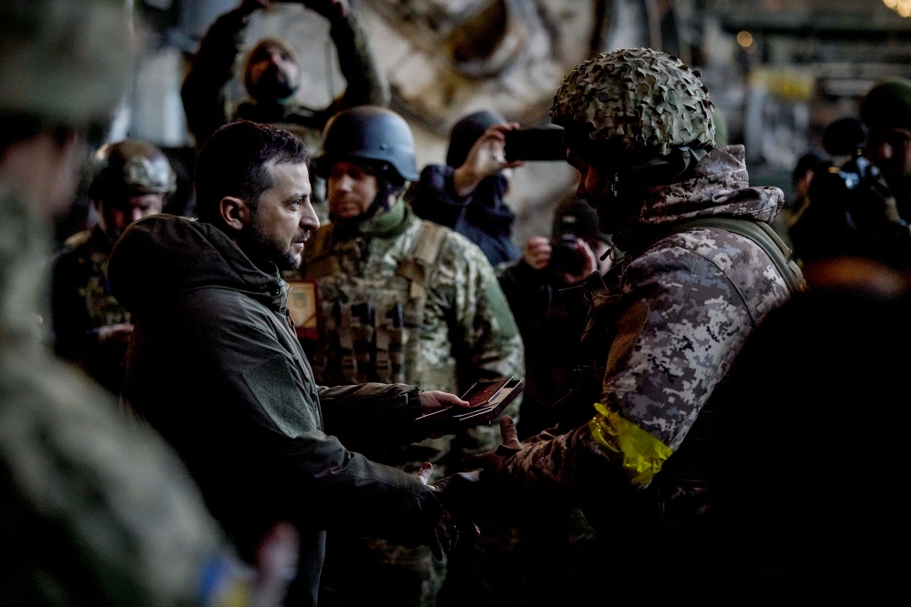 In this handout picture taken and released on December 20, 2022 by the Ukrainian Presidential press services Ukraine President Volodymyr Zelensky (left) hands out the State Award to a soldier during a medal giving ceremony to Ukrainian servicemen who have been holding back a fierce and months-long Russian military campaign for the city, as part of Zelensky's visit in the eastern frontline city of Bakhmut, now the epicentre of fighting in Russia's nearly 10-month invasion of Ukraine. (Photo by STRINGER / UKRAINIAN PRESIDENTIAL PRESS SERVICE / AFP)