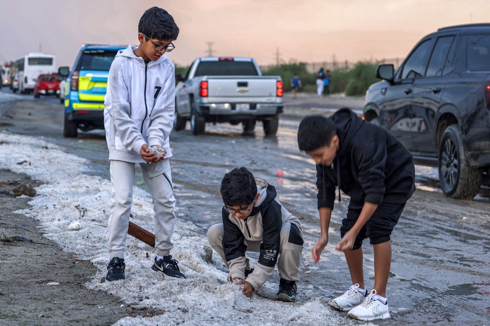 Children toss handfuls of hail particles picked up off the side of a road after a storm in the Umm al-Haiman district, on December 27, 2022. (Photo by Yasser Al-Zayyat / AFP)