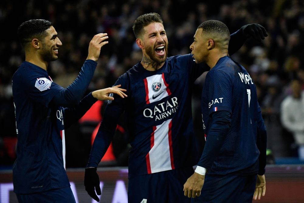 Paris Saint-Germain's French forward Kylian Mbappe (R) celebrates after scoring a penalty with Paris Saint-Germain's Moroccan defender Achraf Hakimi (L) and Paris Saint-Germain's Spanish defender Sergio Ramos in Paris on December 28, 2022. (Photo by Julien De Rosa / AFP)