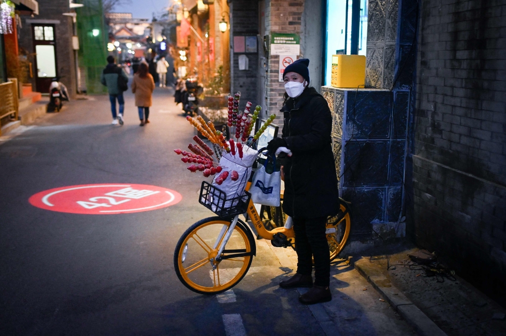 A snacks vendor waits for customers on a street in Beijing on January 2, 2023. (Photo by Wang Zhao / AFP)