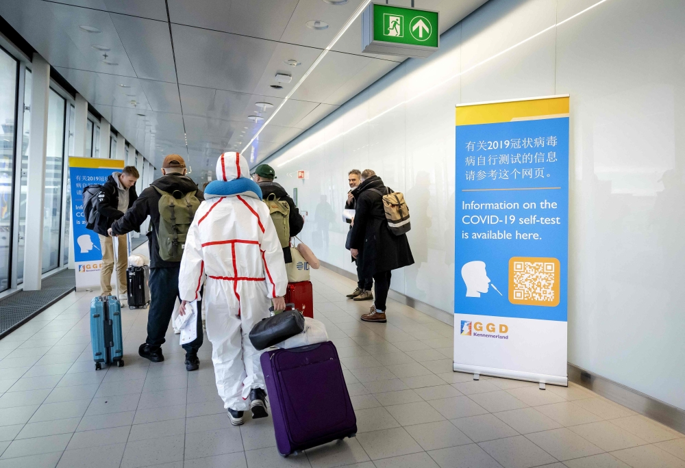 Travelers arriving from China walk past information banners and receive free Covid-19 self-test kits, at Amsterdam's Schiphol Airport on January 4, 2023. (Photo by Robin van Lonkhuijsen / ANP / AFP)