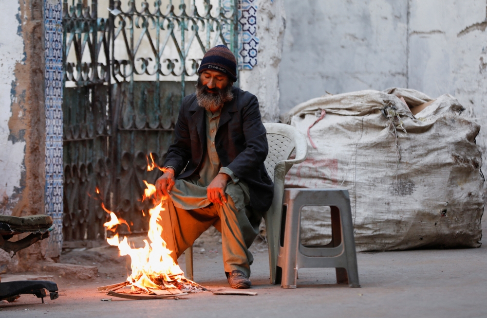 A man keeps himself warm near a fire during early morning hours along a street in Karachi, Pakistan, January 4, 2023. (REUTERS/Akhtar Soomro)