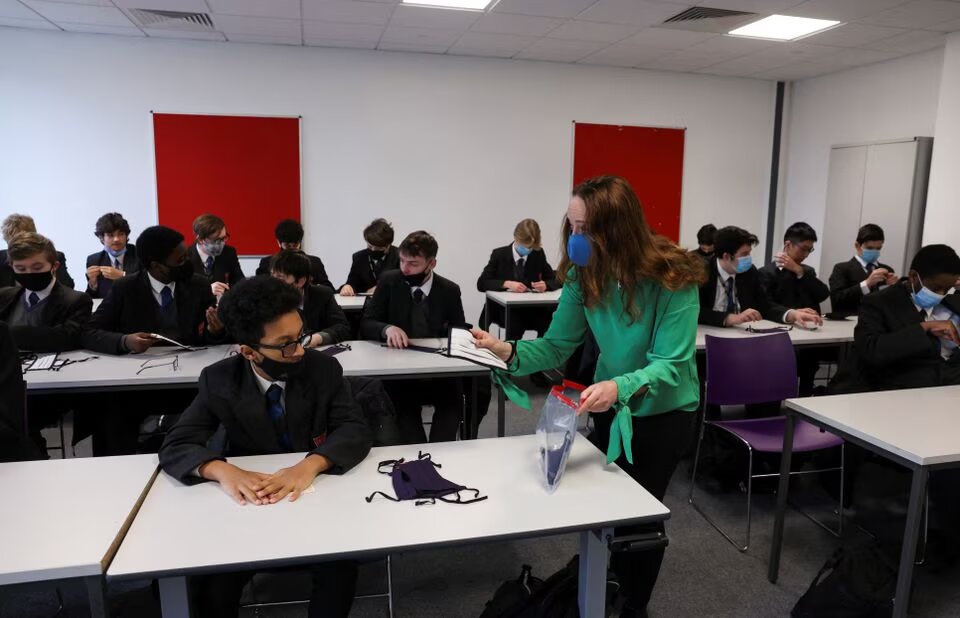 A teacher hands out face masks to students on the first day back at school, as the coronavirus disease (COVID-19) lockdown begins to ease, at Fulham Boys School in London, Britain, on March 8, 2021. File Photo / Reuters
