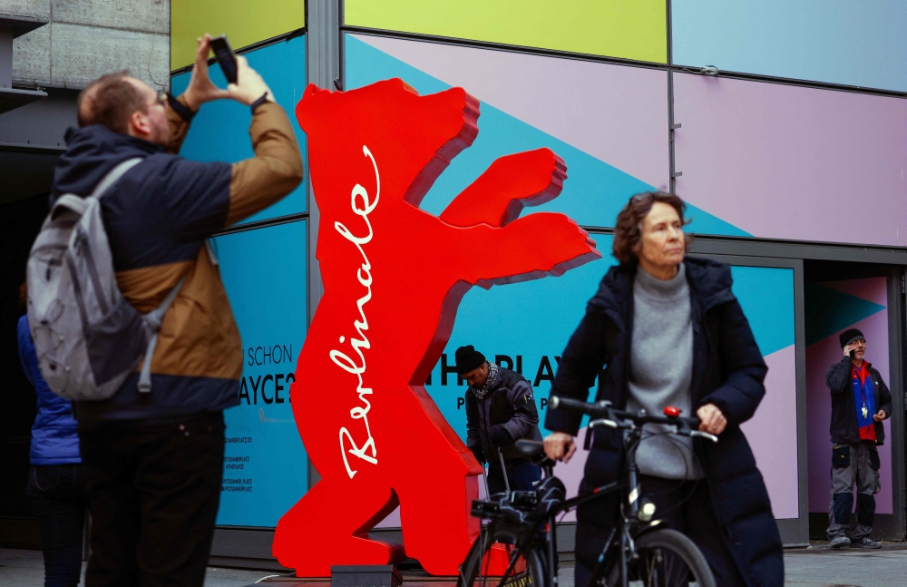 A man makes a photograph as a woman passes the logo of the upcoming Berlinale 73rd International Film Festival in Berlin on February 15, 2023. (Photo by David GANNON / AFP)