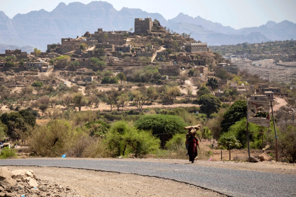 A woman carrying tree branches to be used as firewood walks along a road, on the outskirts of Taez, in Yemen, on February 24, 2023. (Photo by AHMAD AL-BASHA / AFP)