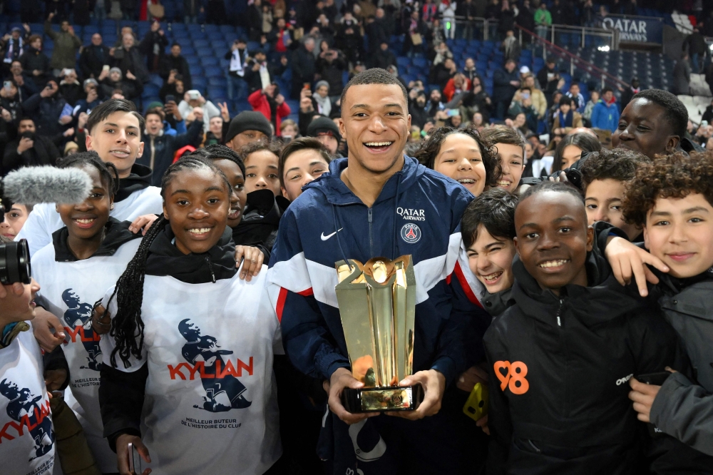 Paris Saint-Germain's French forward Kylian Mbappe poses with a trophy and children at the end of a ceremony after he became Paris Saint-Germain's all-time top scorer on March 4, 2023. (Photo by Franck Fife / AFP)