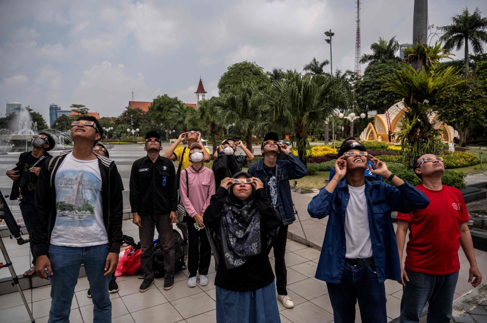 People watch a partial solar eclipse in Surabaya on April 20, 2023. (Photo by Juni Kriswanto / AFP)