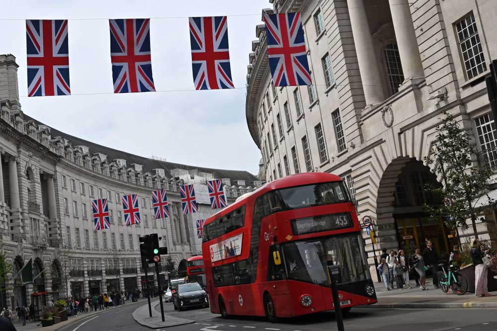 A red London bus passes beneath Union flags on Regent Street, in central London, on April 30, 2023 ahead of the coronation ceremony of Charles III and his wife, Camilla. (Photo by Justin Tallis / AFP)