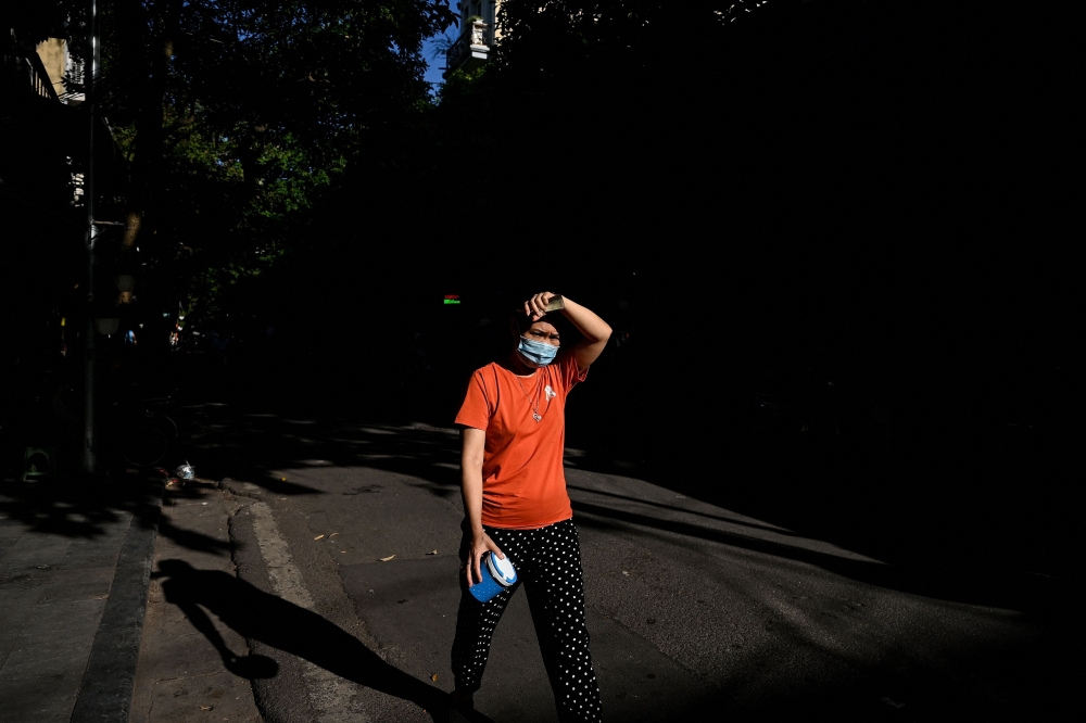 In this file illustration photo taken on June 18, 2021, a woman wearing a face mask shields her face from the sun while walking along a street in the old quarters of Hanoi. Photo by Manan VATSYAYANA / AFP