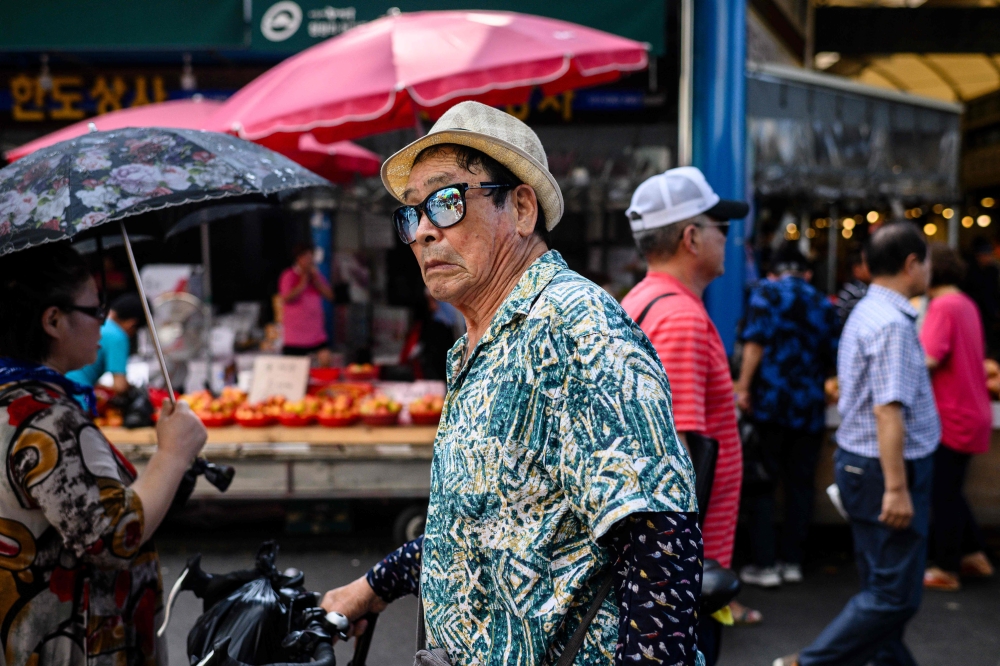 :A man wearing a hat and sunglasses walks along a street during a hot day in Seoul on August 4, 2023. (Photo by ANTHONY WALLACE / AFP)
