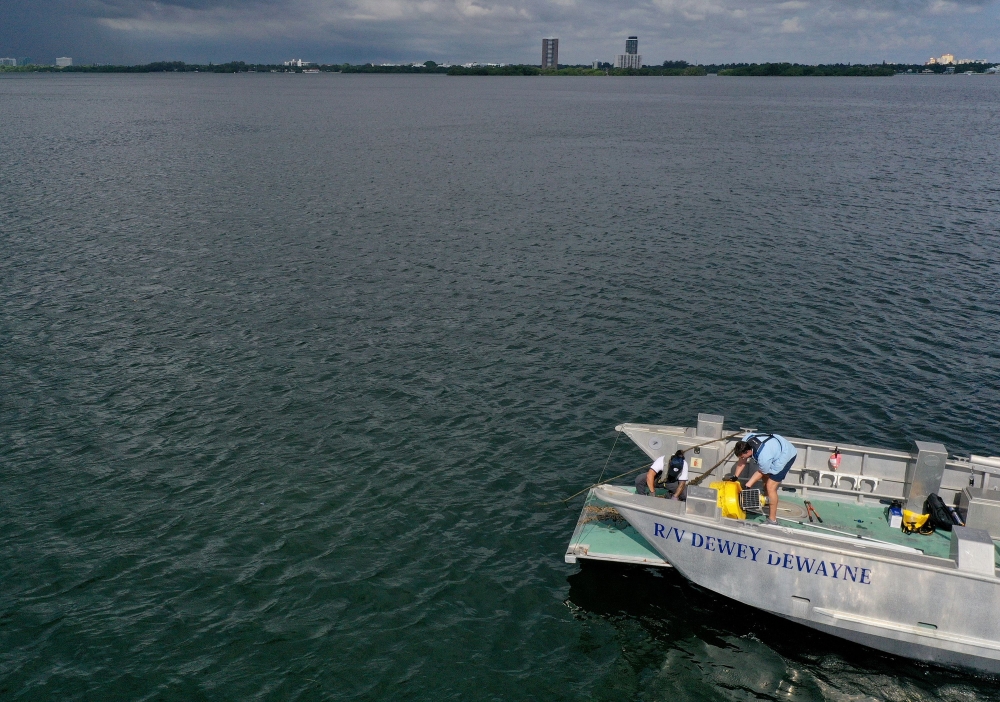 :MIAMI, FLORIDA - AUGUST 03: In an aerial view, (L-R) Nick Evans and Bradley Schonhoff conduct routine maintenance on a research buoy in Biscayne Bay on August 03, 2023 in Miami, Florida. (Photo by JOE RAEDLE / GETTY IMAGES NORTH AMERICA / Getty Images via AFP)
