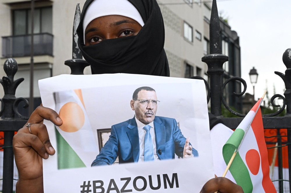 A woman holds the image of ousted Niger President Mohamed Bazoum, 63, who has been held by coup plotters with his family in his official Niamey residence since July 26, during a protest outside the Niger Embassy, in Paris on August 5, 2023. (Photo by Stefano Rellandini / AFP)