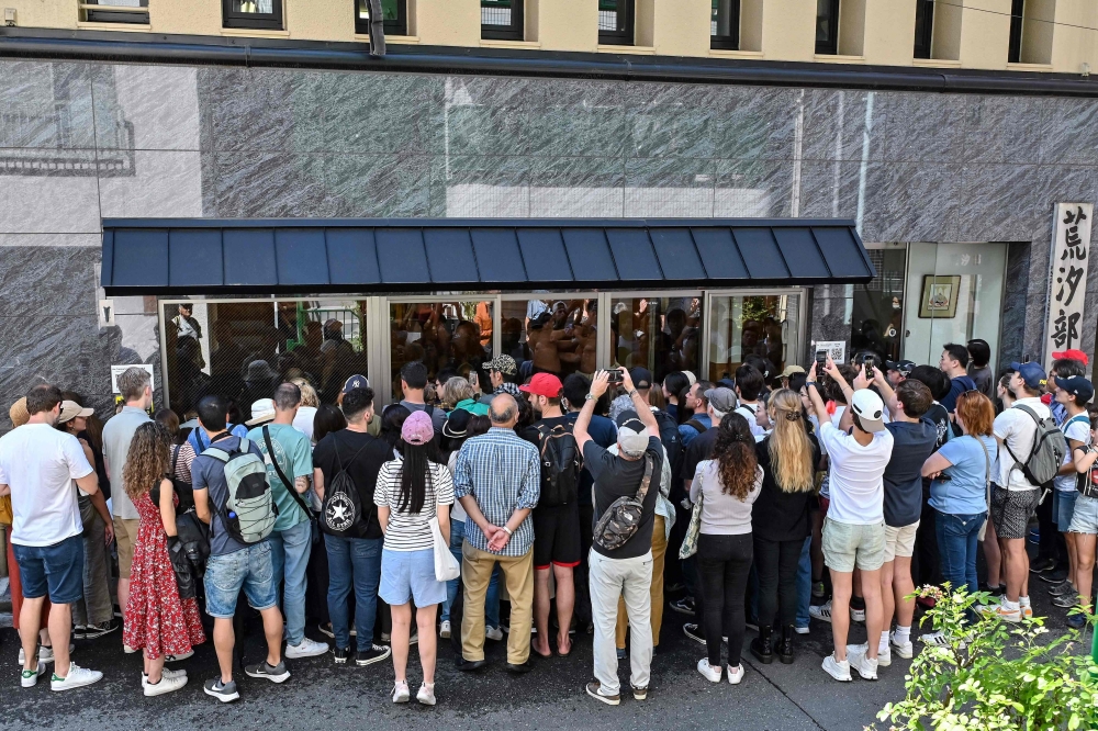 This photo taken on June 7, 2023 shows a group of people, many of them tourists, trying to watch a sumo training session through the glass windows at the Arashio-beya sumo stable in Tokyo. (Photo by Richard A Brooks / AFP)