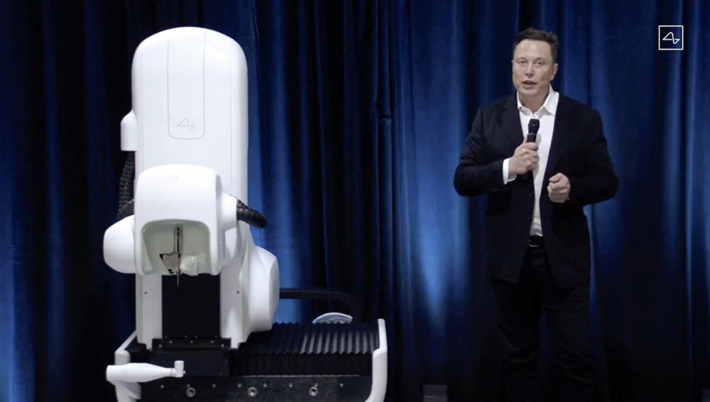 This video grab made from the online Neuralink livestream shows Elon Musk standing next to the surgical robot during his Neuralink presentation on August 28, 2020.(Photo by Neuralink / AFP) 

