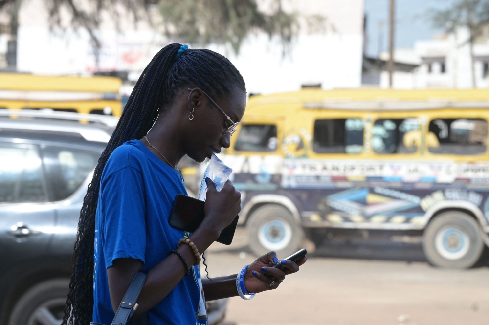 A woman drinks from a plastic sachets filled with drinkable water in Dakar, on August 25, 2023. Photo by SEYLLOU / AFP