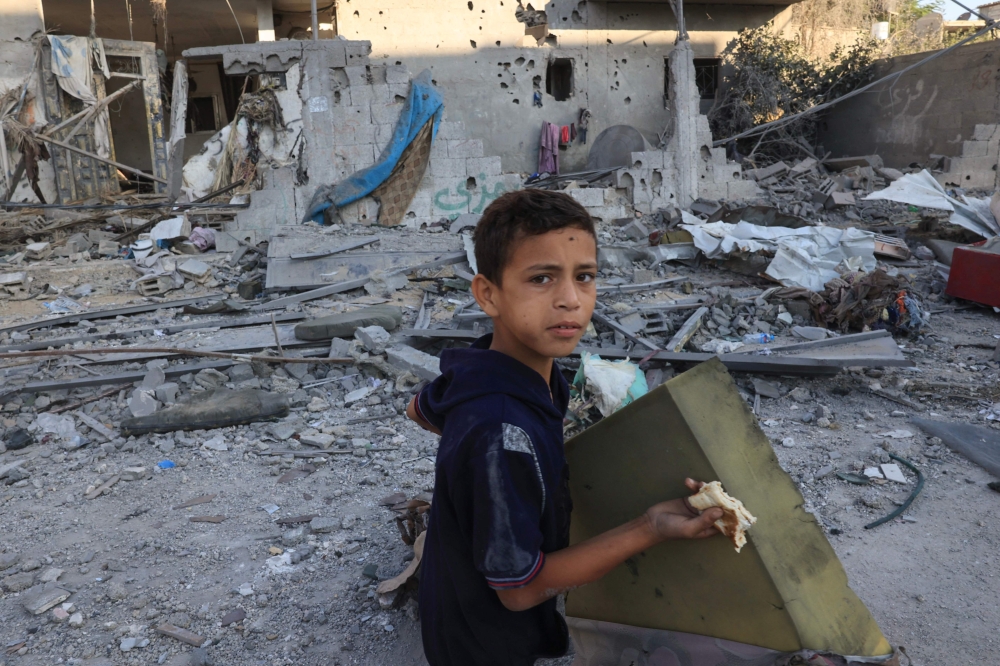 A Palestinian boy salvages belongings from a destroyed home following Israeli bombardment in Rafah in the southern Gaza Strip, on October 18, 2023. (Photo by Said Khatib / AFP)