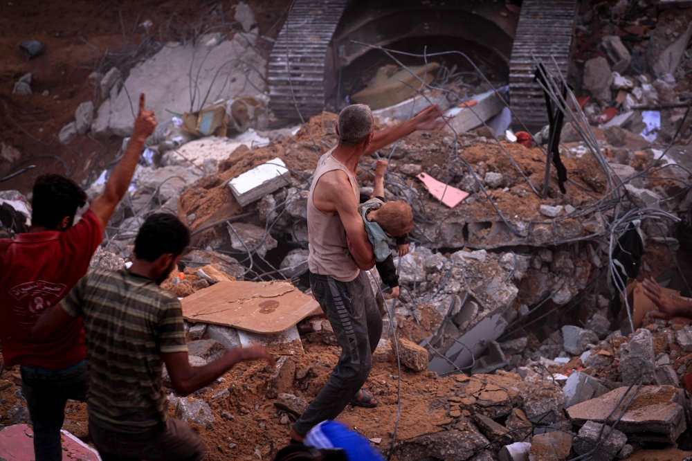 A Palestinian man carries the body of a child after being unearthed from the rubble of a building in the Nuseirat refugee camp on October 31, 2023. (Photo by Mahmud Hams / AFP)