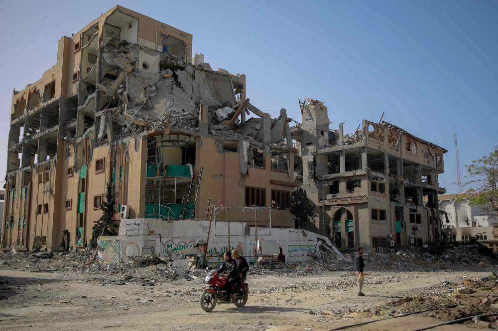 Palestinians drive a motocycle past the destroyed building of the Islamic University in Gaza City on November 26, 2023 (Photo by Omar El-Qattaa / AFP)
