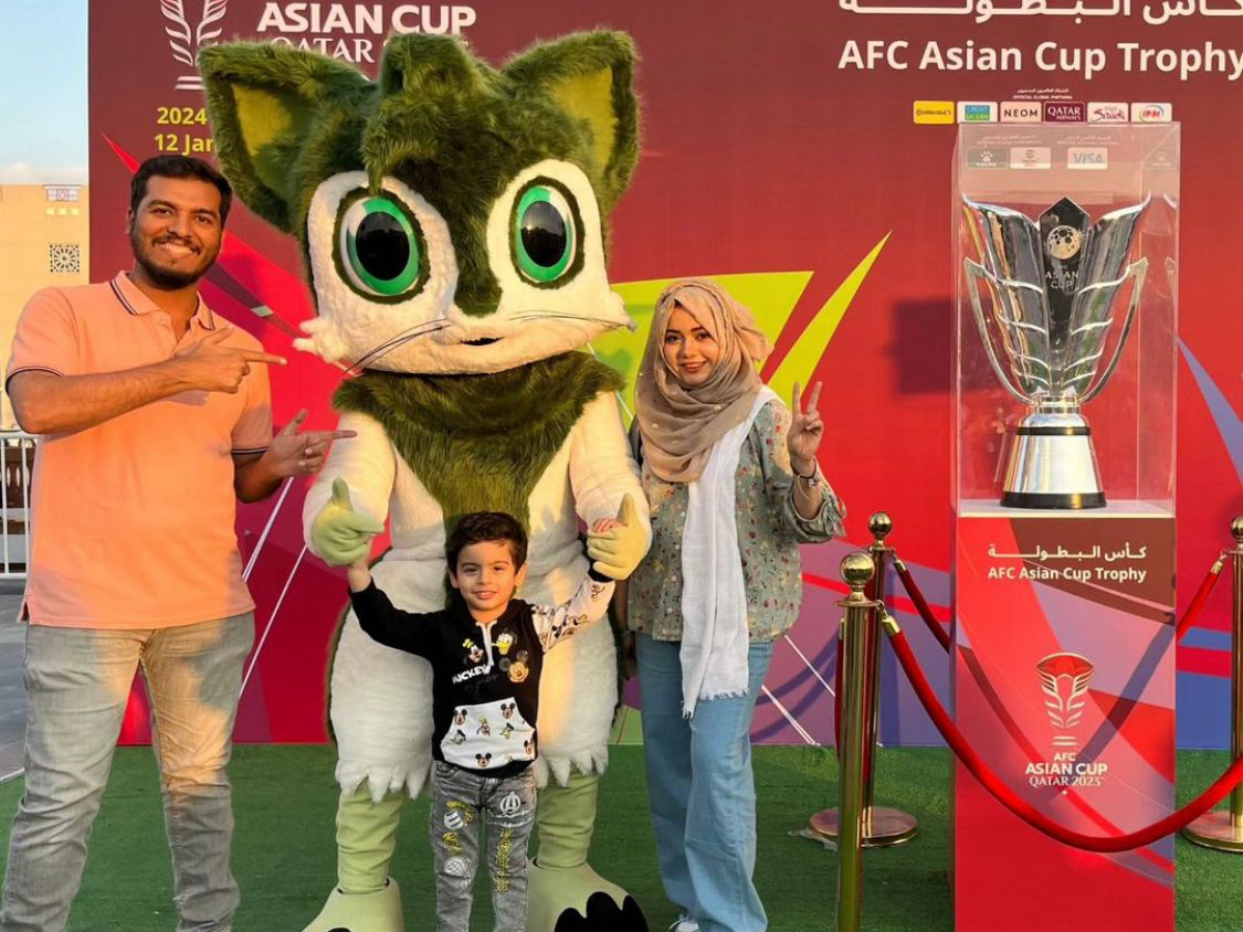 A family of three pose for a photograph alongside the AFC Asian Cup champions trophy and Zkriti, one of the mascots.