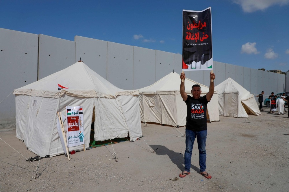 A man lifts a placard near tents set up by volunteers and NGO workers along the Egyptian side of the Rafah border crossing, demanding clearance for an aid convoy to enter the Gaza Strip, on October 19, 2023. (Photo by Kerolos Salah / AFP)