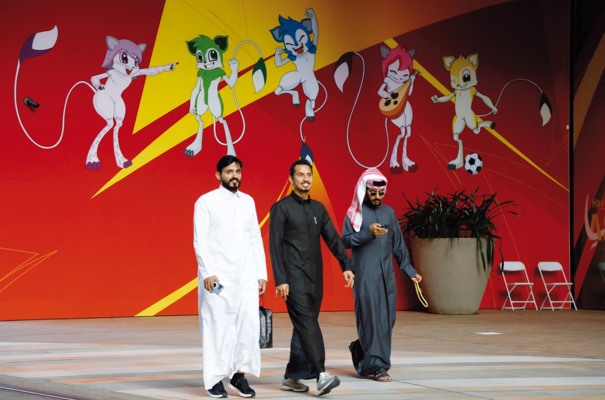 People walk near a wall displaying the five desert rodents, the official mascots of the AFC Asian Cup Qatar 2023. AFP