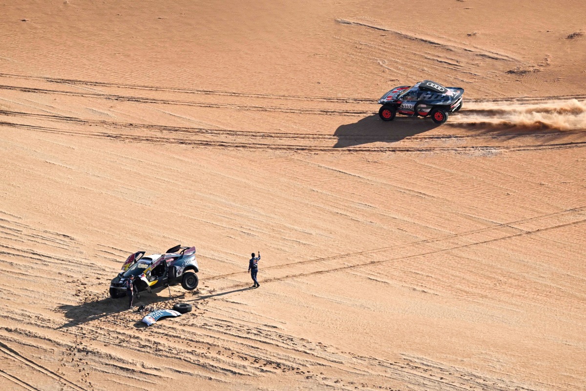 Nasser Racing’s Qatari driver Nasser Al Attiyah waves to Team Audi Sport’s Spanish driver Carlos Sainz as he stands by his car following a mechanical failure in the dunes yesterday. AFP