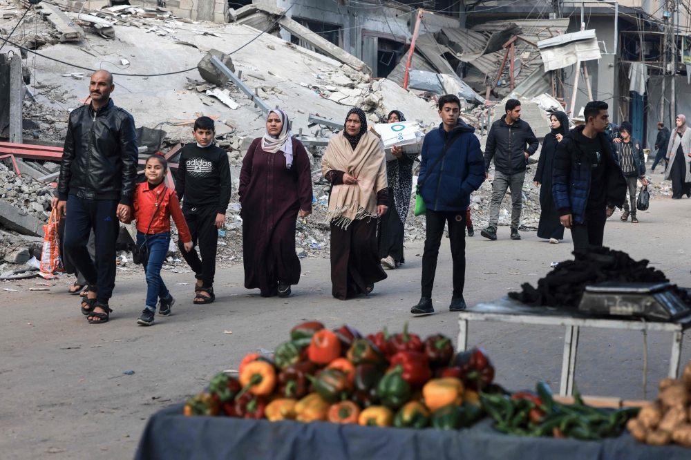 People walk past destroyed buildings in Rafah on the southern Gaza Strip on January 14, 2024. Photo by AFP