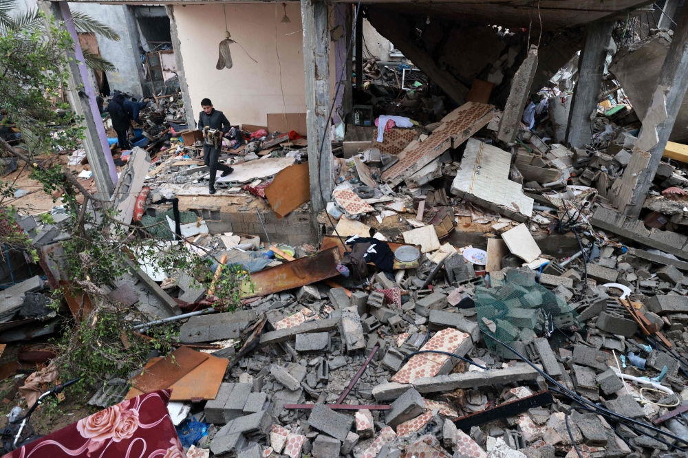 A young man salvages objects amid the rubble of a building destroyed by Israeli bombing in Rafah in the southern Gaza Strip on January 27, 2024. (Photo by AFP)
