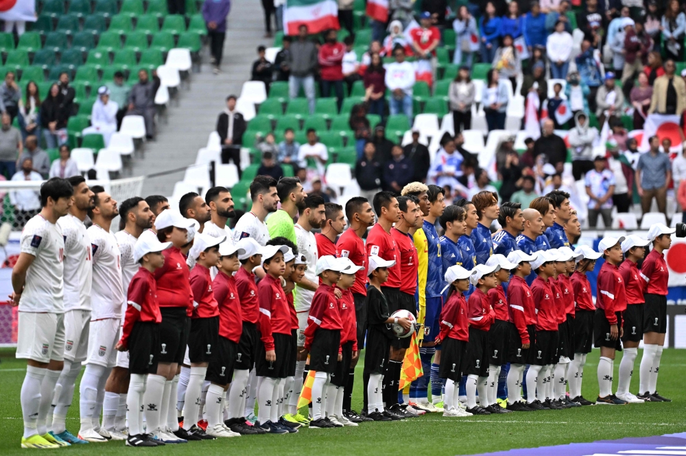 Japan's players (in blue) and Iran's players (in white) stand for their national anthems before the start of the Qatar 2023 AFC Asian Cup quarter-final football match at Education City Stadium. (Photo by Hector Retamal / AFP)