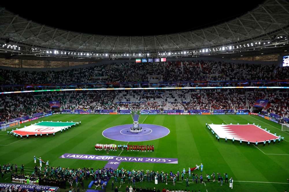 Qatar's players (center R) and Iran's players (center L) line-up in front of a large-scale Qatar 2023 AFC Asian Cup trophy replica before the start of the Qatar 2023 AFC Asian Cup semi-final football match between Iran and Qatar at al-Thumama Stadium in Doha on February 7, 2024. Photo by KARIM JAAFAR / AFP