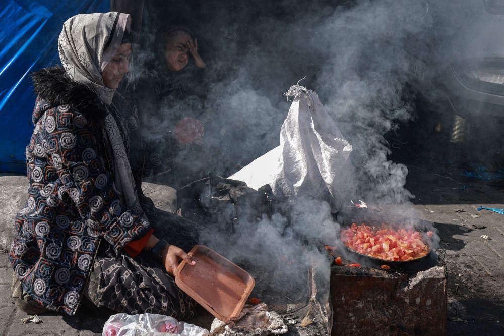 A displaced Palestinian woman uses a makeshift stove to cook a meal on the street in Rafah in the southern Gaza Strip on February 11, 2024, amid the ongoing conflict between Israel and the Palestinian militant group Hamas. (Photo by Mohammed Abed / AFP)