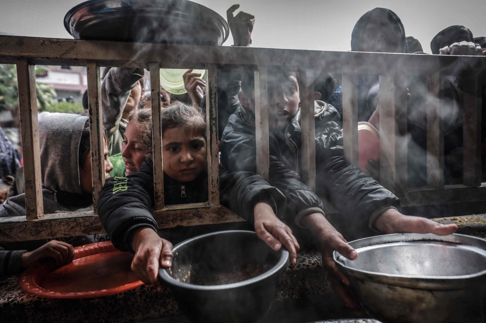 Displaced Palestinian children gather to receive food at a government school in Rafah in the southern Gaza Strip on February 19, 2024. (Photo by Mohammed Abed / AFP)