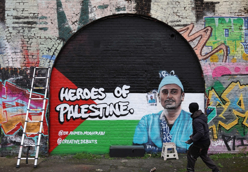 A photograph taken on February 20, 2024 in south east London shows a graffiti artist working to create a street art image of Dr Ahmed Moghrabi, a surgeon at the Nasser Hospital in Khan Younis, southern Gaza, as part of a project by the art platform Creative Debuts called 