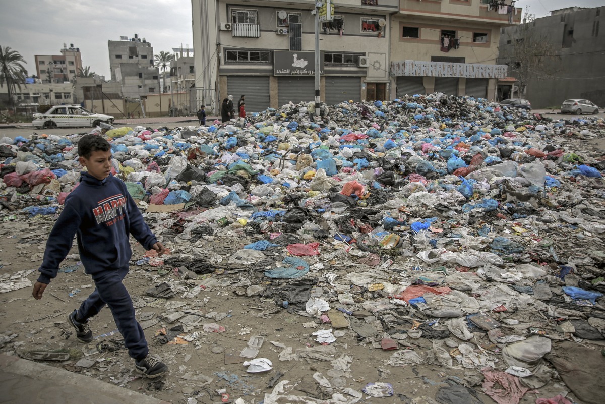 A Palestinian boy walks along a street dumped with garbage in Gaza City on February 24, 2024. Photo by AFP