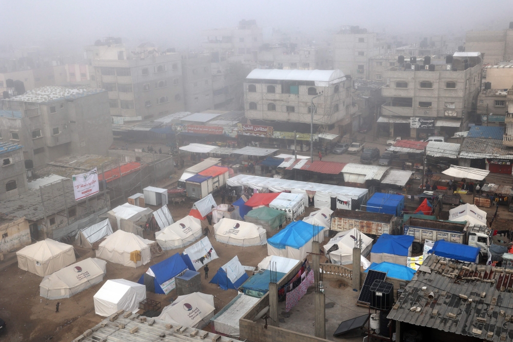 Fog covers buildings and tents set up by displaced Palestinians in Rafah in the southern Gaza Strip on February 25, 2024. (Photo by Said Khatib / AFP)