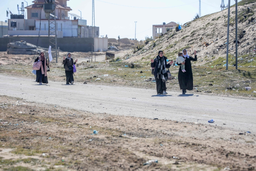 Displaced Palestinian women carrying their belongings lift a white flag as they walk with raised hands past Israeli forces while fleeing the Hamad City area in Khan Yunis in the southern Gaza Strip on March 5, 2024. (Photo by AFP)