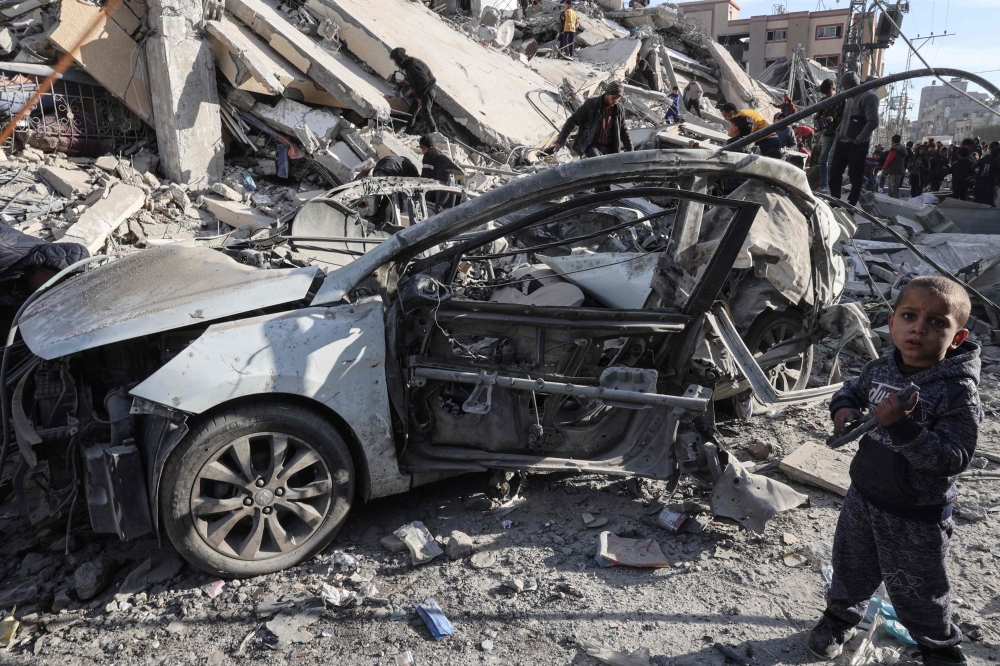 A young Palestinian boy stands next to a wrecked car in the rubble of a residential building hit in an overnight Israeli air strike in Rafah in the southern Gaza Strip on March 9, 2023, amid continuing battles between Israel and the Palestinian militant group Hamas. (Photo by SAID KHATIB / AFP)
