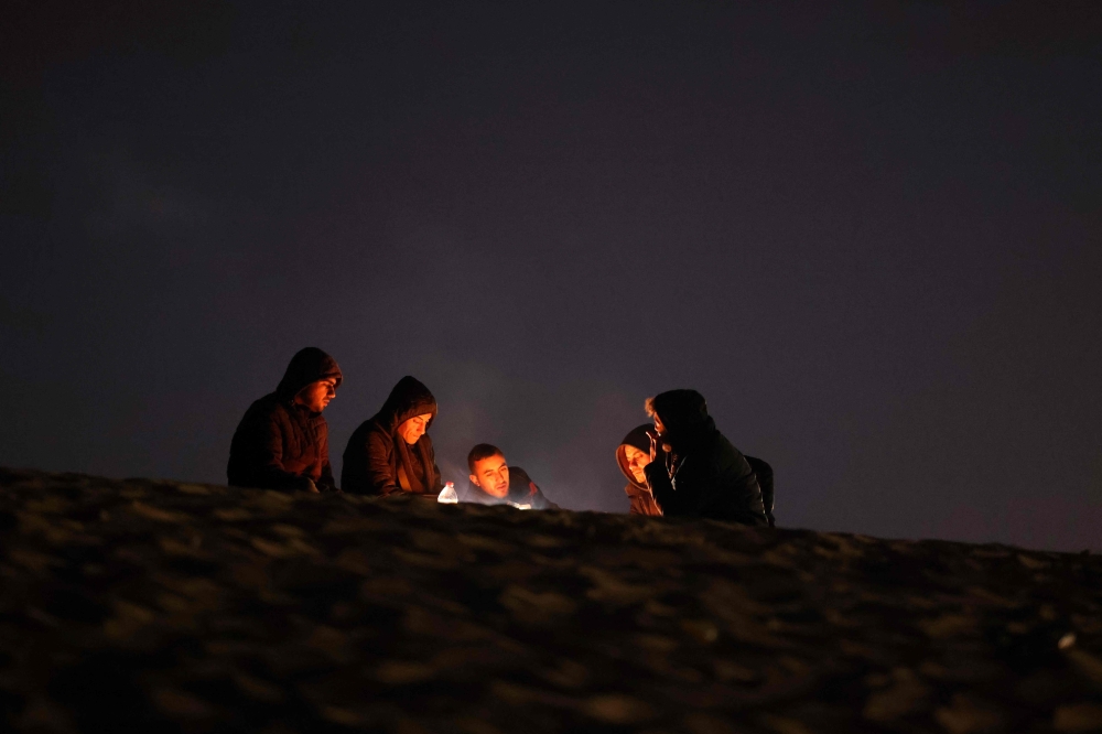 People sit by the fire at a camp for displaced Palestinians in Rafah, in the southern Gaza Strip, on the eve of the holy month of Ramadan on March 10, 2024. Photo by MOHAMMED ABED / AFP