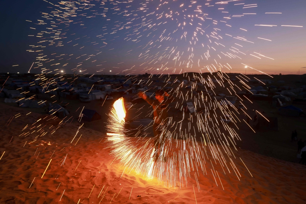 A Palestinian youth plays with a sparkler in Rafah, in the southern Gaza Strip, on the eve of the Muslim holy fasting month of Ramadan on March 10, 2024, amid ongoing battles between Israel and the Palestinian group Hamas. (Photo by MOHAMMED ABED / AFP)
