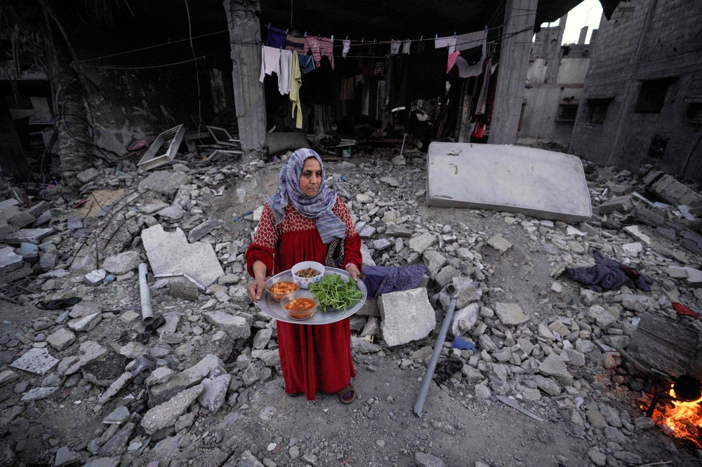 A Palestinian woman prepares to serve an iftar meal, the breaking of fast, amidst the ruins of her family's house, on the first day of the Muslim holy fasting month of Ramadan, in Deir el-Balah in the central Gaza Strip on March 11, 2024, amid ongoing battles between Israel and the Palestinian group Hamas. (Photo by AFP)
