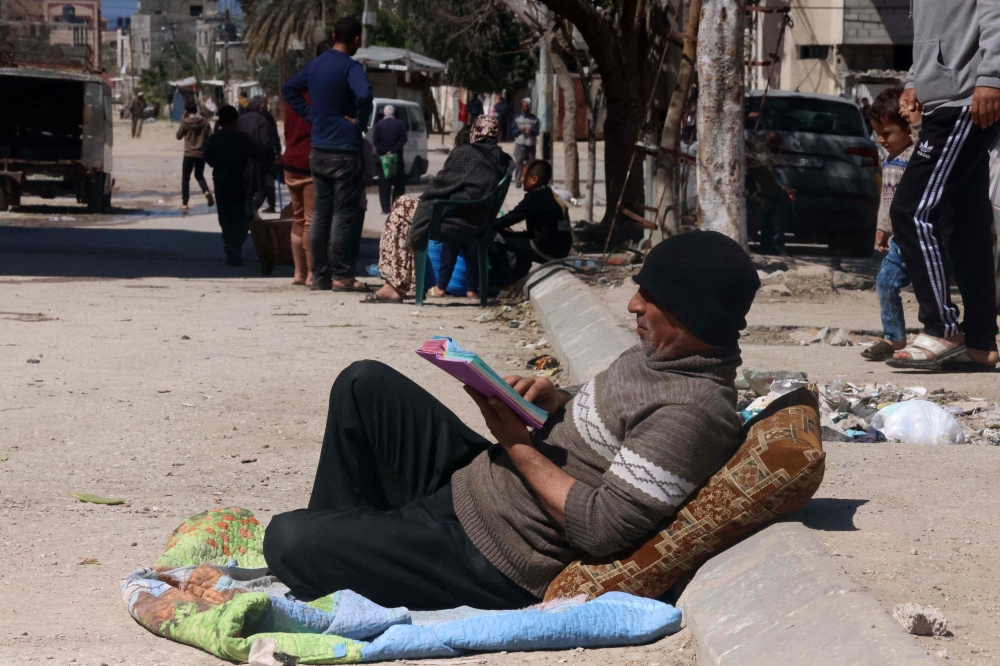 A Palestinian man sits reading in a street in Rafah in the southern Gaza Strip on March 15, 2024, amid ongoing battles between Israel and the militant group Hamas. (Photo by MOHAMMED ABED / AFP)
